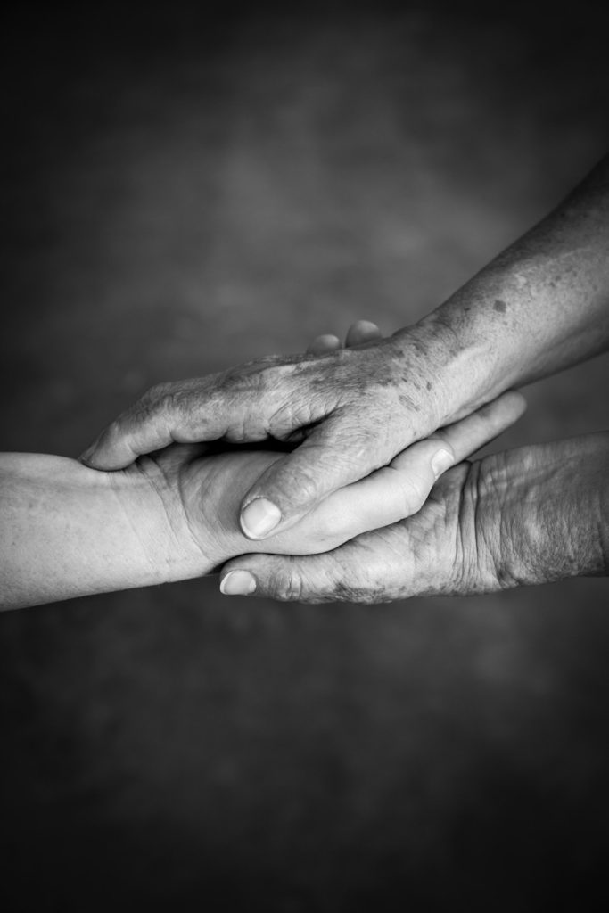 Two hands of an elderly person hold the hand of a younger person